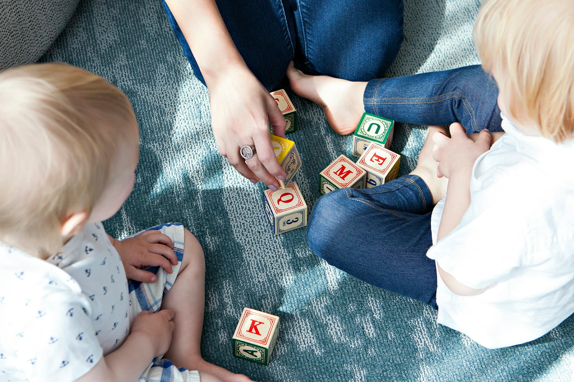 An adult and two toddlers playing with wooden alphabet blocks